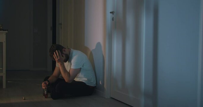 Sad Drunk Adult male sits on home floor drinking alcohol Alone at night 4k