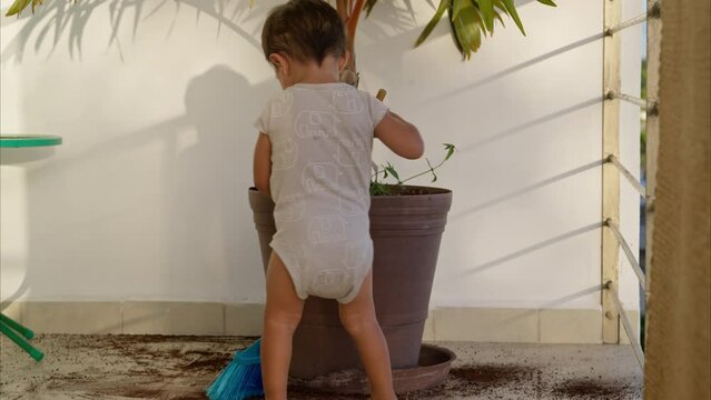 Little young latin toddler in a baby romper sweeping with a toy broom the dirt from the floor after a mischief