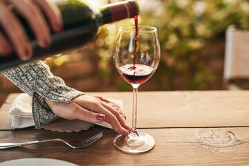 Glass, bottle and hand of woman pouring wine at a table, calm and content while enjoying free time on a patio. Red wine, hands and lady relax with luxury drink, enjoy a relaxing weekend alone at home