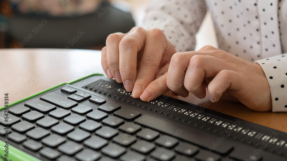 Wall mural a blind woman uses a computer with a braille display and a computer keyboard. inclusive device.