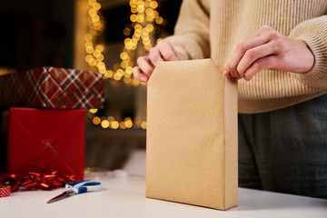 Woman in warm sweater packaging gift box with craft paper. Present for holiday event. Surprise for...