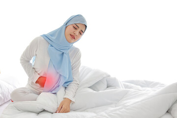 Menstrual pain or stomachache young asian muslim woman sitting on bed. Beautiful girl hold stomach and feeling painful with unhappy face. Healthy concept