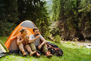 White young couple drinking tea resting by tent in green forest