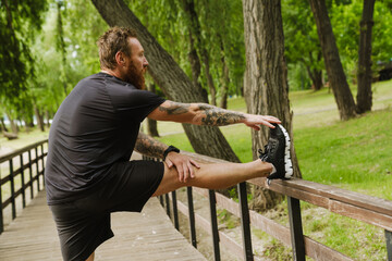 Sideview of young handsome tattooed bearded man stretching his leg