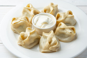 Russian meat dumplings with sour cream on white plate