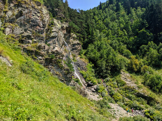 Fototapeta na wymiar Arkhyz, Karachay-Cherkessia, Russia - August 25, 2022: Beautiful view of the Baritovy waterfall flowing down from the cliff. People admire nature. Caucasus mountains