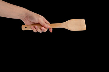 hand holding a wooden spatulas for cooking on black background.