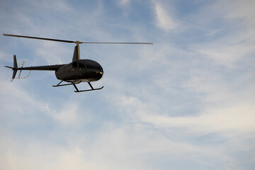 Black helicopter  in air over blu sky and white clouds