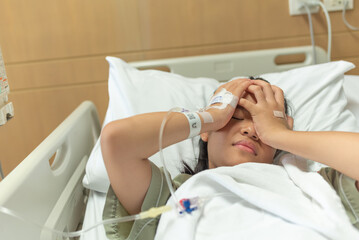 Asian woman patient with medical drip have headache with migraine headaches hospital ward, teenager sick in hospital with saline intravenous, Selective focus, healthcare and health insurance concept.
