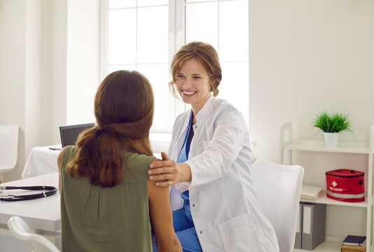 Friendly doctor in a white coat supporting a teenage child. Happy beautiful young woman who works as a pediatrician at the clinic talks to a school girl, reassures her, smiles and touches her shoulder