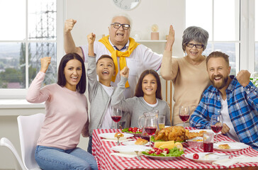 Fototapeta premium Yeah we finally gathered together. Happy cheerful mom, dad, grandma, grandpa and kids celebrating family event at home, sitting at table with chicken or turkey, enjoying festive dinner and having fun