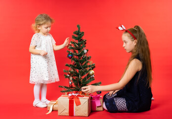 Girls, children with gifts and christmas trees. Christmas. Studio. Red background