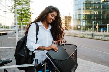 Young woman putting folder in basket while riding bicycle on street
