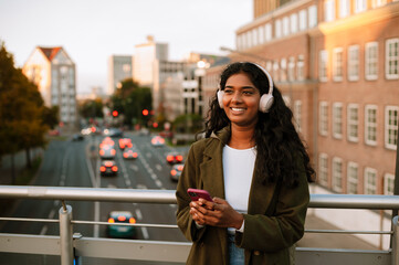 Obraz premium Young woman using headphones and cellphone while walking on city street