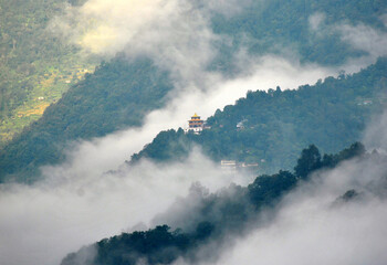 A panoramic view of fog and mist covered array of hills and Buddhist monastery in the centre at Ranka looks mesmerizing as seen from Gangtok opposite of it in Sikkim, India.