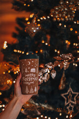 Female hands holding a cup of coffee or tea with a Christmas design. Winter holiday decor, New Year details, golden bokeh