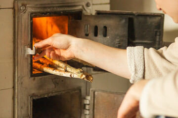 Adult man putting firewood, birch branches in the old stove indoors at home. Man's hand putting log to wood burning oven