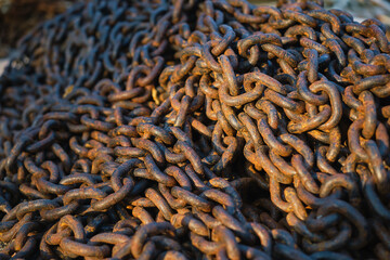 Rusty anchor chain is dumped on the pier, close-up selective focus. Heap of old heavy rusty chain links idea for background