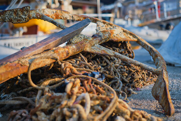 Old rusty anchor on the anchor old chain in the marina of the city in the rays of the rising sun. Pier at the yacht club, selective focus, background or screen about seaside vacation and travel