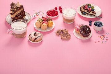 Fototapeta na wymiar Table with various cookies, donuts, cakes, coffee cups on pink background.