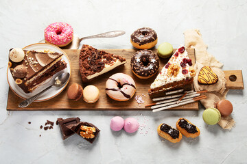 Table with various cakes, cookies, donuts and coffe cups on light background.