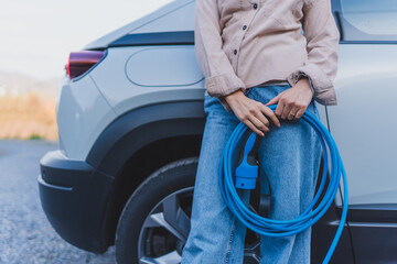 Close-up of woman holding power supply cable from her electric car, prepared for charging it in...