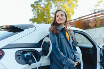 Young woman waiting while her electric car charging in home charging station, sustainable and...
