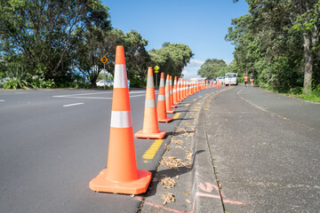 Orange traffic cones along the road, blurred people walking on the footpath. Auckland.