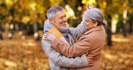 Happy senior couple in love looking at each other with tenderness, dancing together in park on autumn day