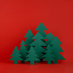 Bright Christmas background - paper green spruce forest on red backdrop in minimalist modern style, copy space, square. New year scene for presentation products, advertising text, card, poster, flyer.