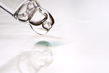 Glass dropper in a drop of cosmetic on a gray background. Concept of making researches in care cosmetics.