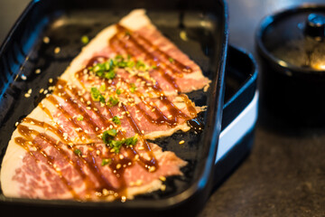 Japanese wagyu beef steak cuts white sesame seeds and sliced spring onions on a black tray