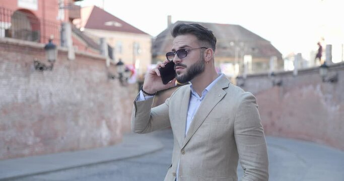 sexy young man having a phone conversation, looking around and moving in front of an old medieval town background