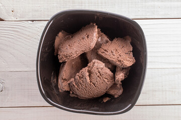 Dark brown chocolate ice cream in a black ceramic bowl on a wooden table, close-up, top view.