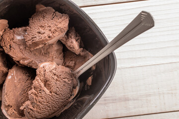 Dark brown chocolate ice cream in a black ceramic bowl on a wooden table, close-up, top view.