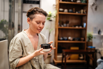 A woman in a coffee shop holds a cup of aromatic coffee or tea in her hands. Evening mood