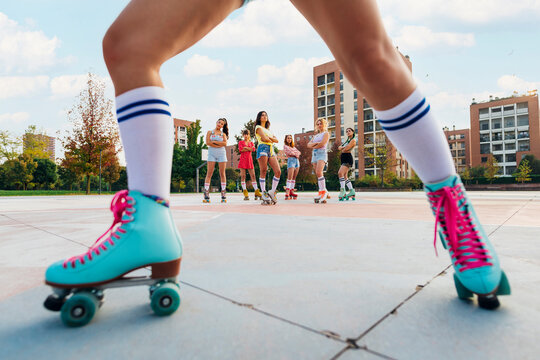 Friends wearing roller skates at sports court seen through woman's leg