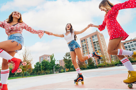 Happy friends holding hands practicing roller skating at sports court