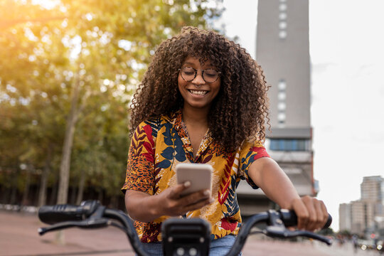 Happy young woman sitting on bicycle and using smart phone