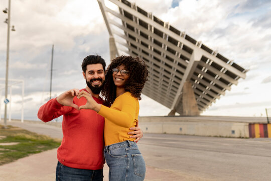 Happy young couple gesturing heart shape in front of solar panels