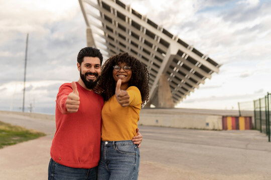 Happy man with woman showing thumbs up gesture in front of solar panels
