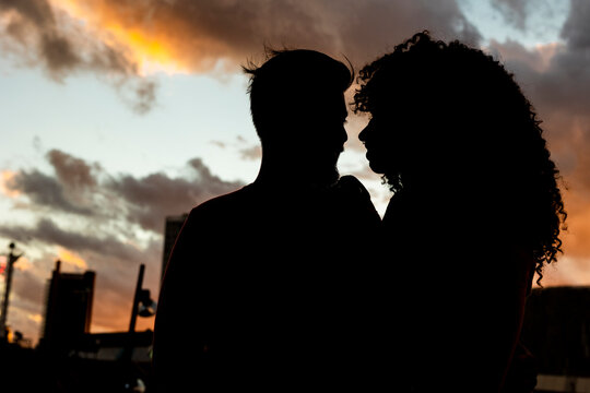 Silhouette of young couple under cloudy sky at sunset