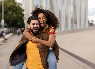 Cheerful young man enjoying and giving piggyback ride to girlfriend at footpath