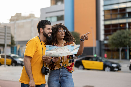 Happy young man with girlfriend holding map and gesturing at footpath