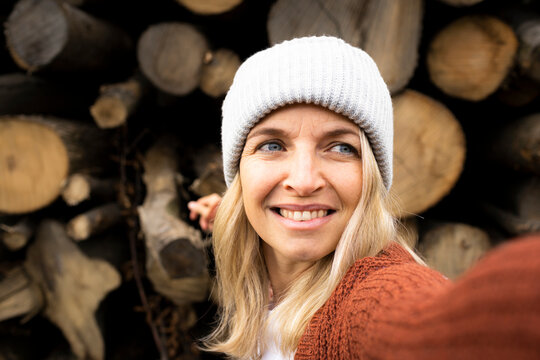 Smiling woman with knit hat day dreaming in front of logs