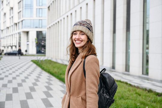Happy woman standing with backpack in front of building