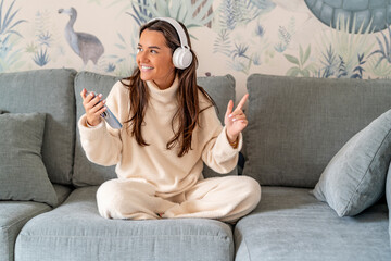 Happy woman wearing wireless headphones listening music on sofa at home