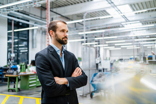 Contemplative businessman with arms crossed standing in factory
