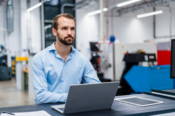 Thoughtful young businessman with laptop at industry