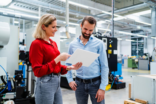 Smiling businesswoman explaining colleague over tablet PC at factory